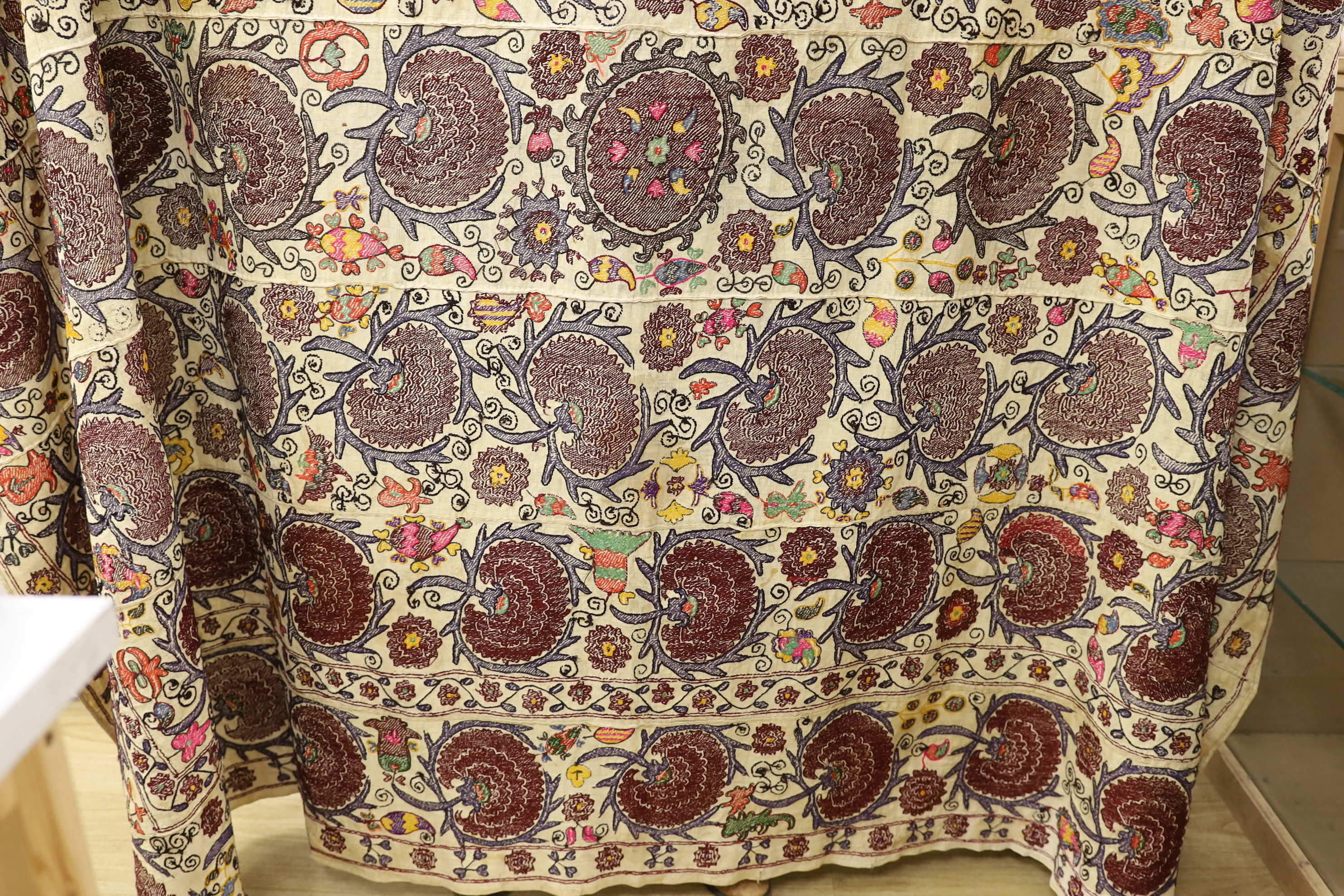 An exceptionally large Suzani hanging, embroidered with rows of stylised aubergine flower heads, the field filled with further polychrome flowers and serrated edged leaves, 190 x 270cm